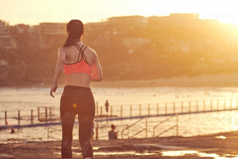 Woman running on beach with sun flare for morning exercise - Australian Stock Image