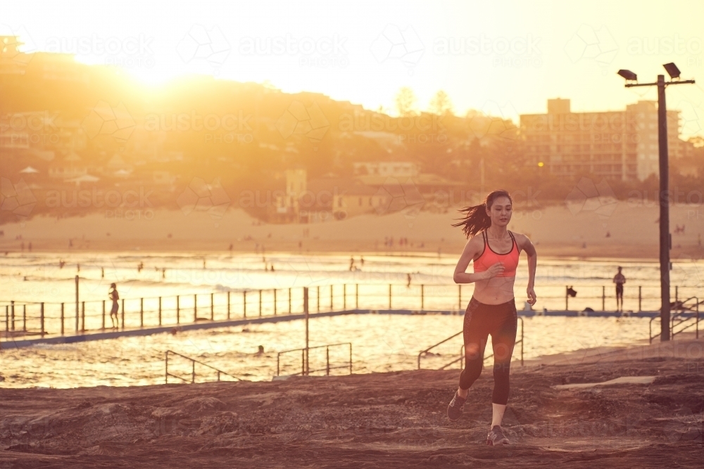 Woman running on beach with sun flare for morning exercise - Australian Stock Image