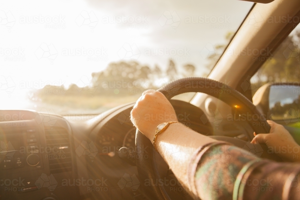 Woman's hands on a car steering wheel with sun flare on highway - Australian Stock Image