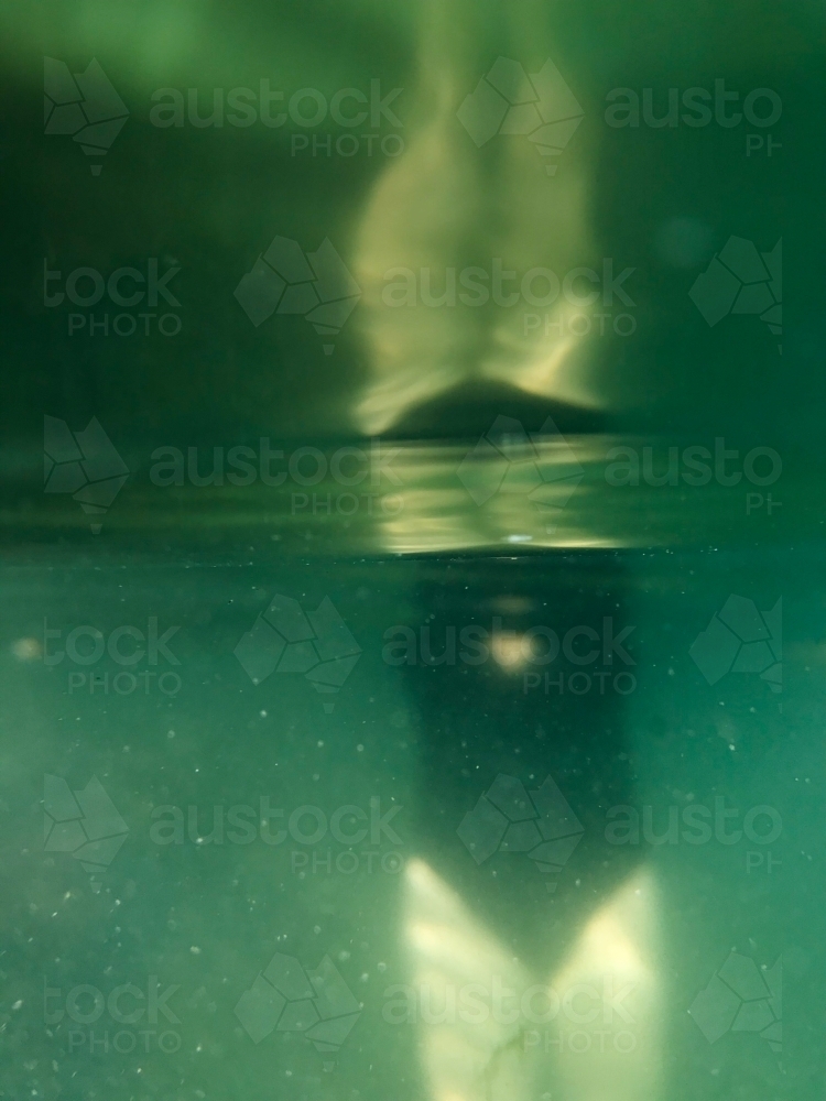 Woman’s torso submerged under ocean with reflection in black full piece swimsuit - Australian Stock Image