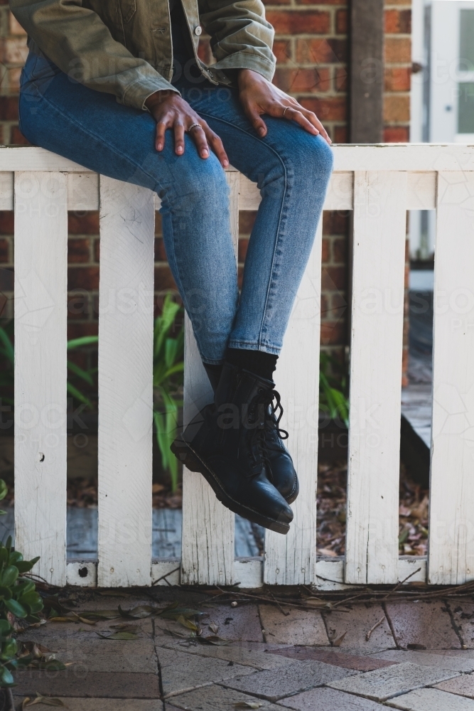 woman sitting fence, wearing jeans and black boots - Australian Stock Image