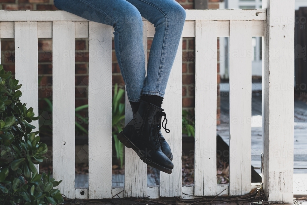 woman sitting fence, wearing jeans and black boots - Australian Stock Image