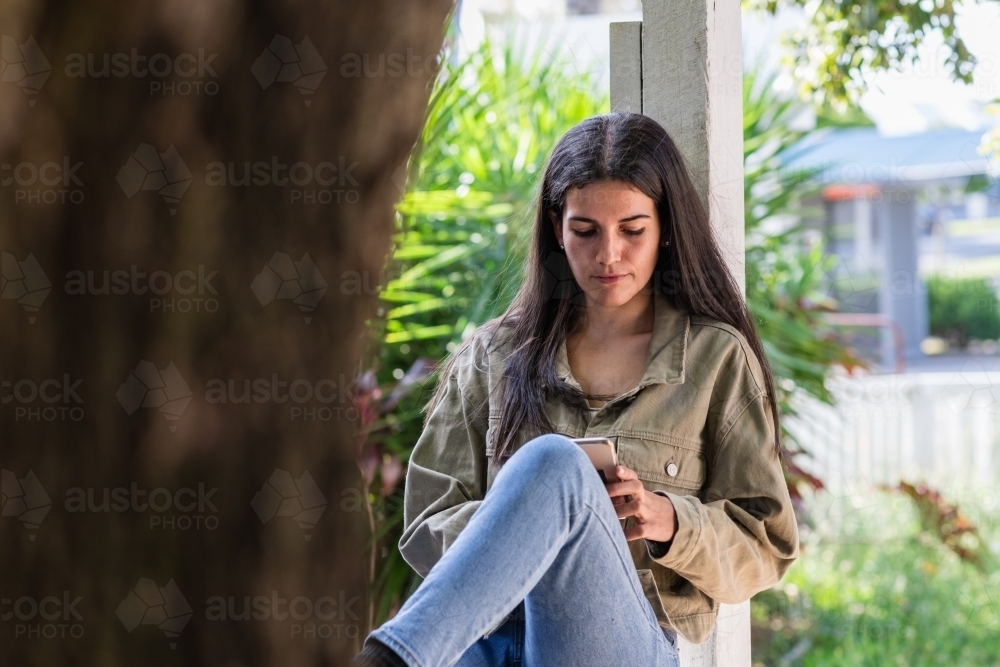 woman sitting fence, wearing jeans and black boots - Australian Stock Image