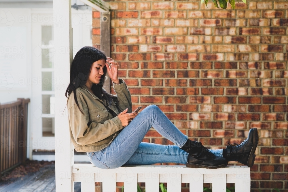 woman sitting fence, wearing jeans and black boots - Australian Stock Image