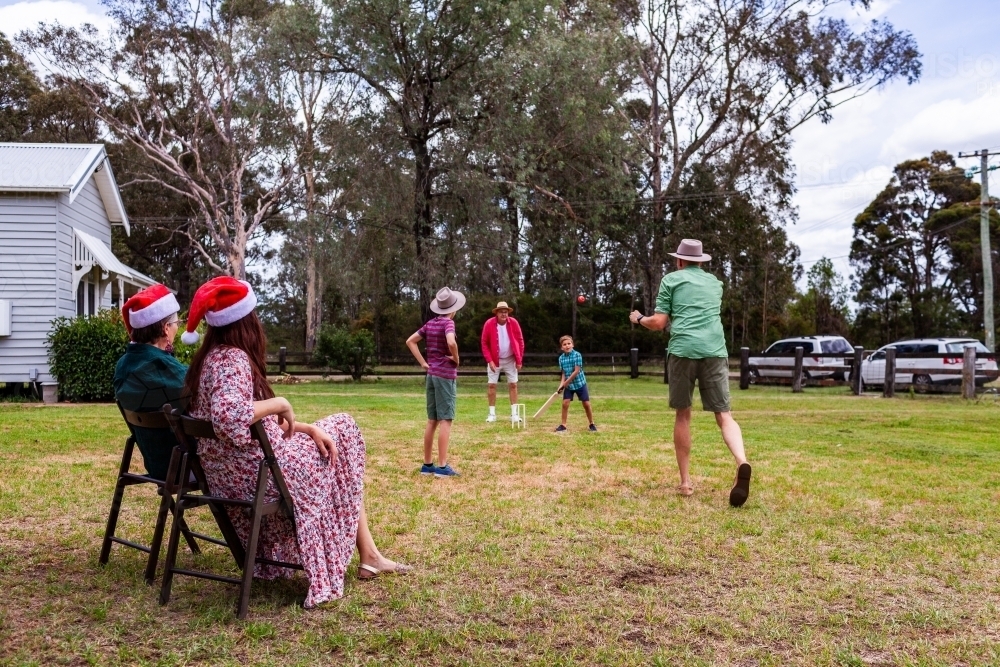 Image of woman sitting in shade watching men and boys play cricket in ...