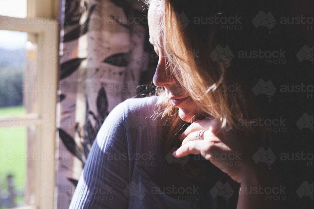 Woman sitting in sunlight at window - Australian Stock Image