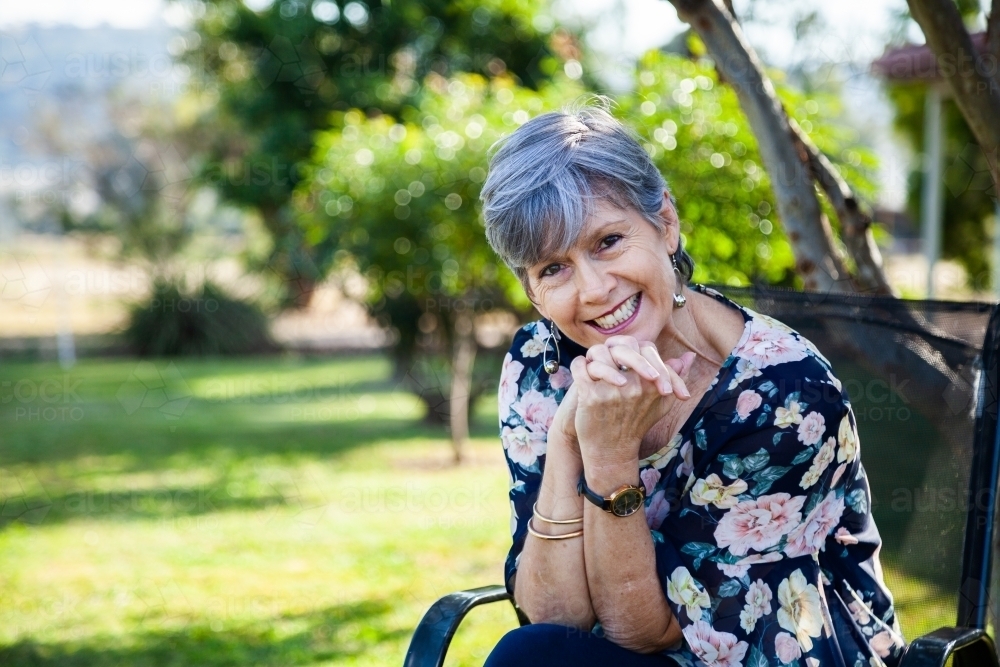 Woman sitting on a chair in garden laughing - Australian Stock Image