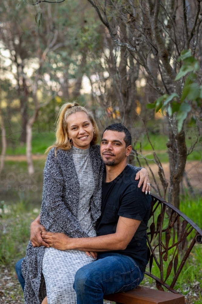 woman sitting on her partner's knee on park bench - Australian Stock Image