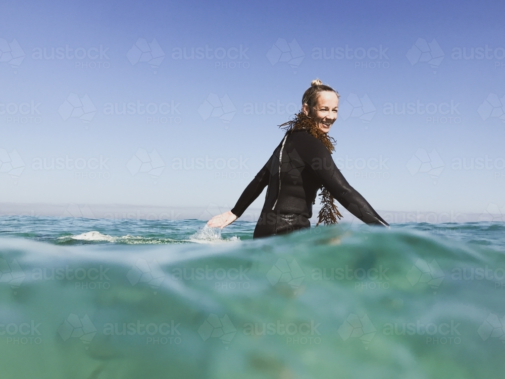 Woman sitting on surfboard paddling arms wearing seaweed - Australian Stock Image