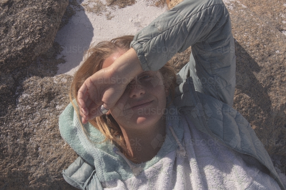 Woman smiling laying on rock on beach covering face from sun - Australian Stock Image