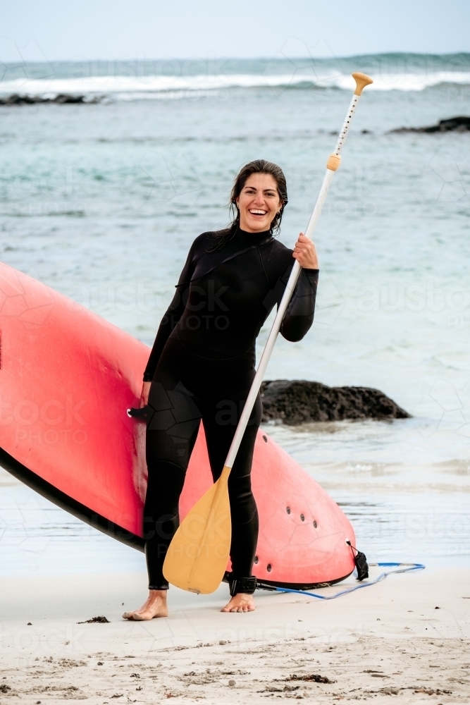 Woman smiling on the beach with a stand up paddle board. - Australian Stock Image