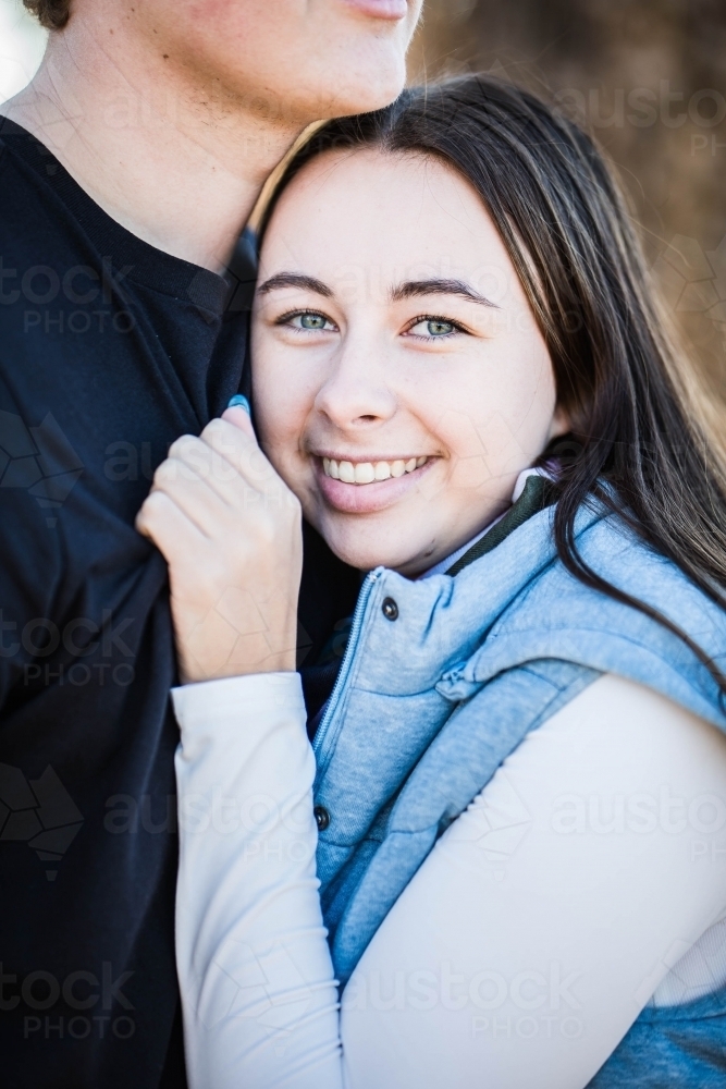 Woman snuggled in to boyfriend's chest smiling hand clutching shirt - Australian Stock Image