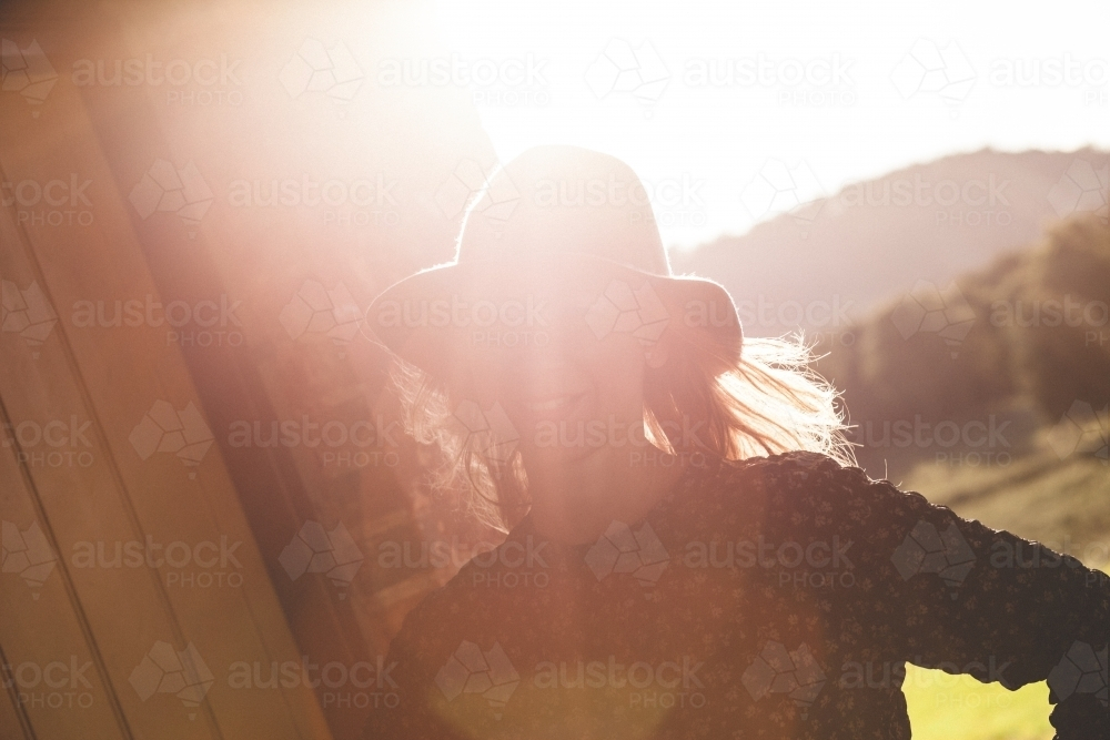 Woman standing on rural porch with sunset behind - Australian Stock Image