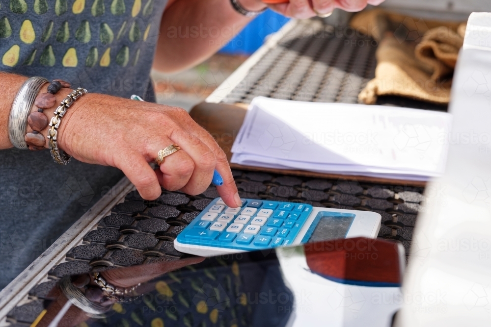 Woman using a calculator to add up numbers and amounts - Australian Stock Image