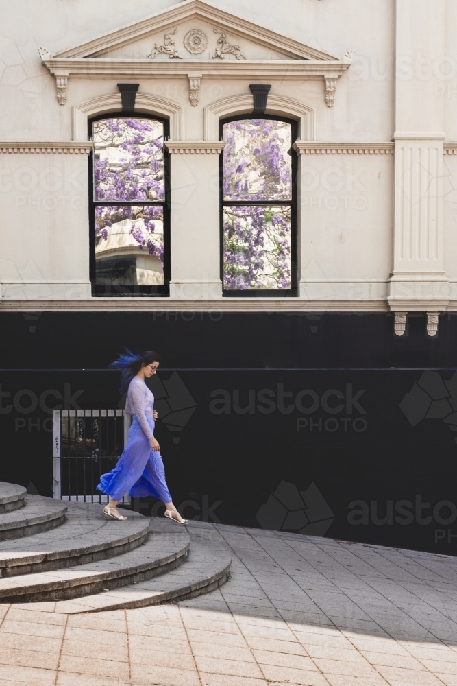 woman walking in the city, jacaranda season - Australian Stock Image