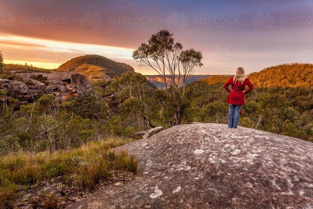 Woman watches first sunlight hit the cliffs and mountain tops - Australian Stock Image