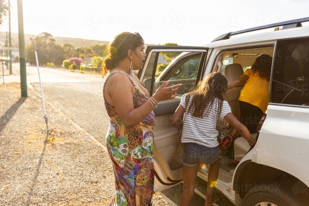 woman watching children getting into the back seat of a four wheel drive vehicle in a street - Australian Stock Image