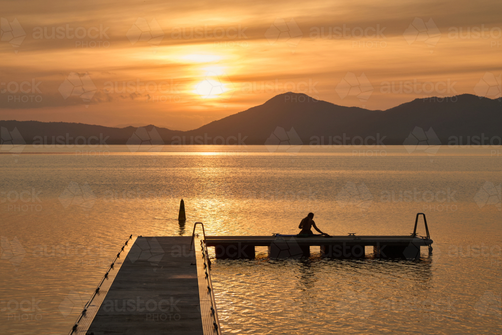 woman watching sunset while sitting on jetty - Australian Stock Image