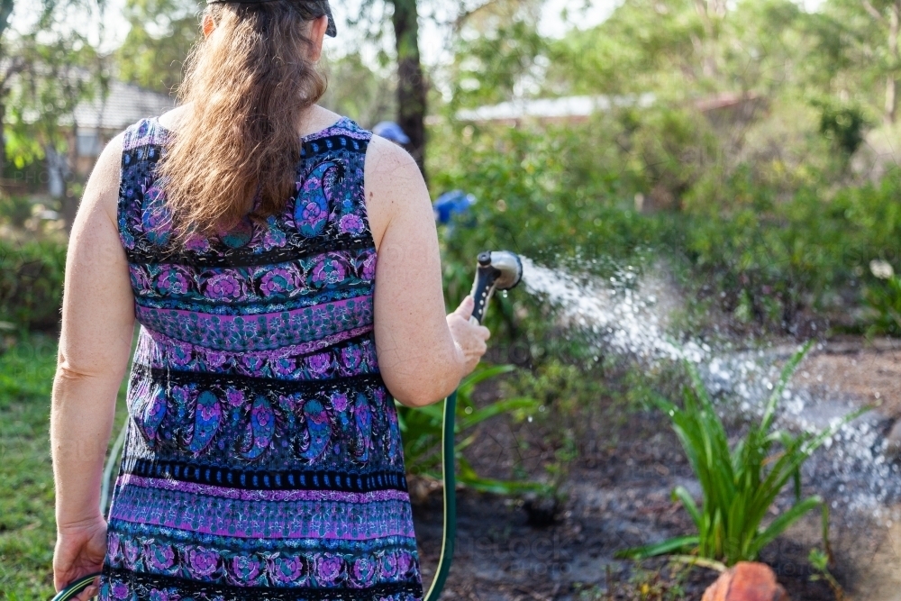 Woman watering garden with hose - Australian Stock Image