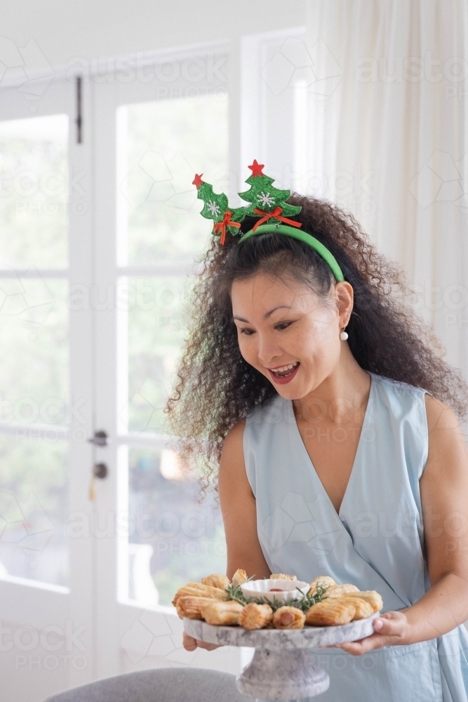 Woman wearing Christmas headband holding platter of pastries - Australian Stock Image