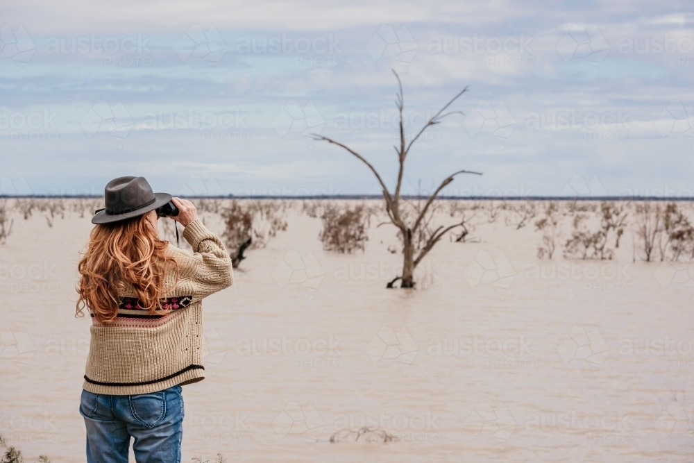 Woman with binoculars looks across the lake. - Australian Stock Image