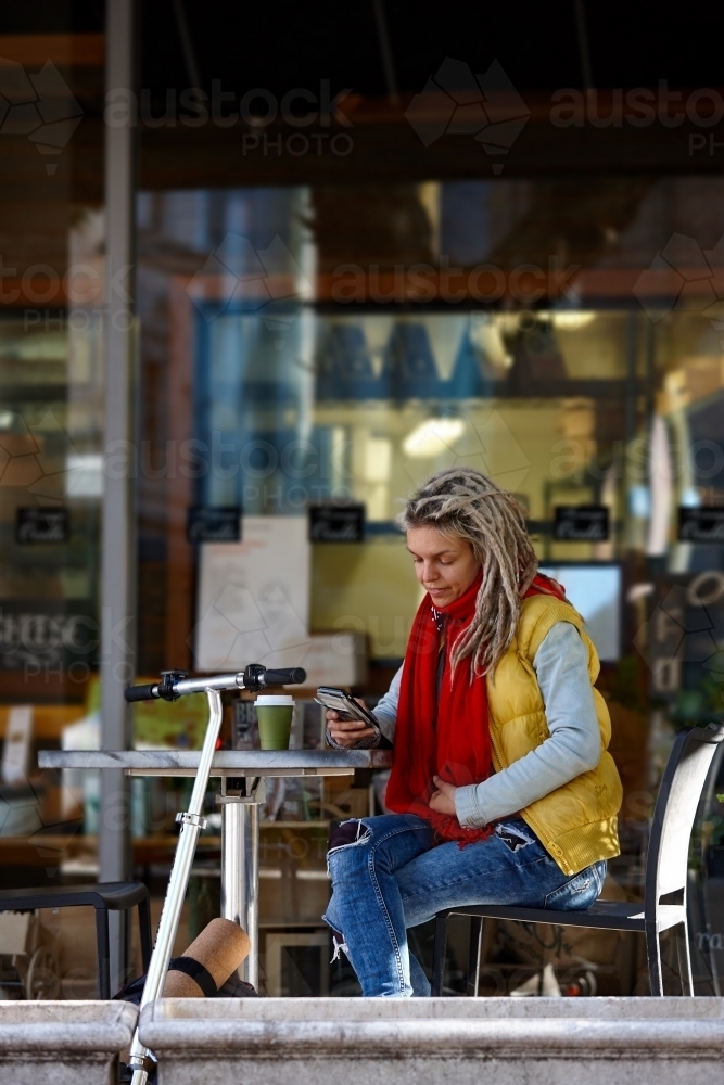 Woman with dreadlocks at cafe with mobile phone and electric scooter - Australian Stock Image