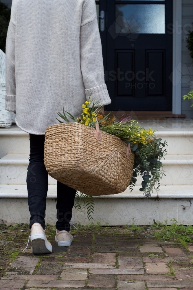 Woman with market basket of wild flowers walking along footpath - Australian Stock Image