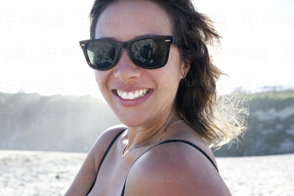 Woman with sunglasses on smiling at the beach - Australian Stock Image