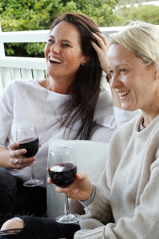 Women laughing on deck with glasses of red wine - Australian Stock Image