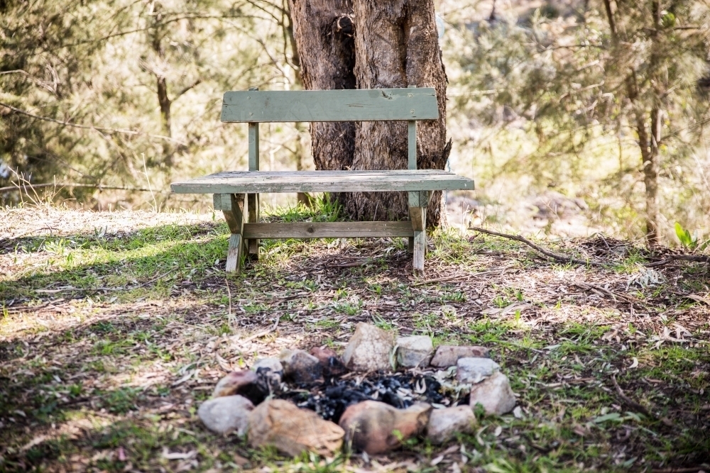 Wooden bench seat in bush with camp fire - Australian Stock Image