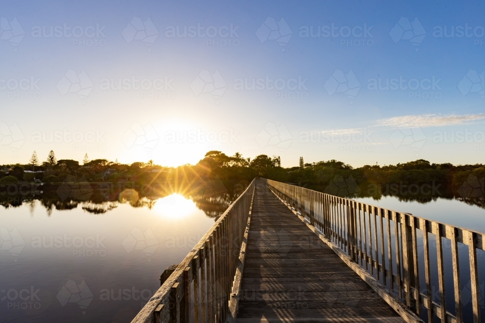 Wooden footbridge leading across Simpsons Creek at Brunswick Heads at sunrise - Australian Stock Image