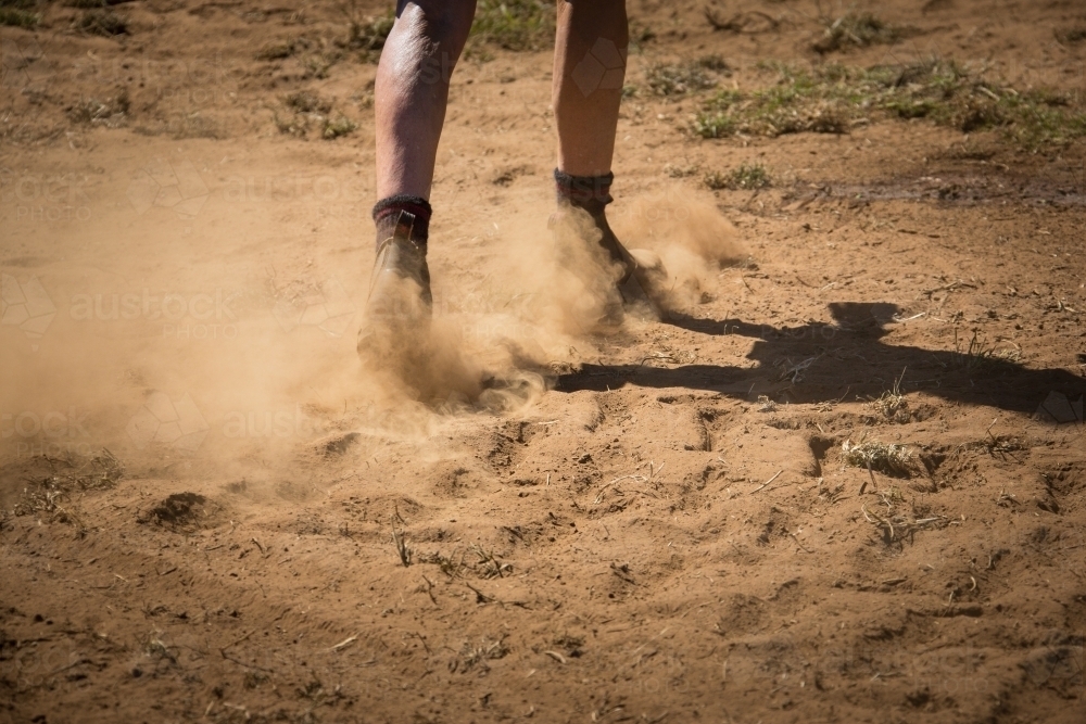 Workboots walking on dusty dry ground - Australian Stock Image