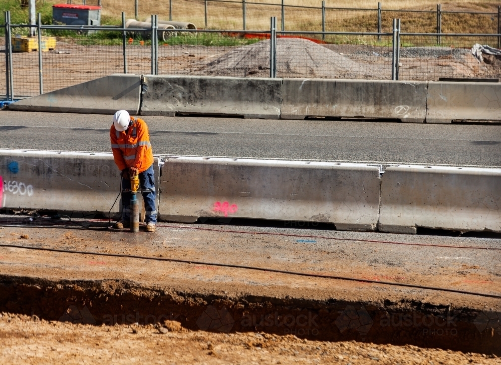 Worker on building site digging hole with machinery - Australian Stock Image