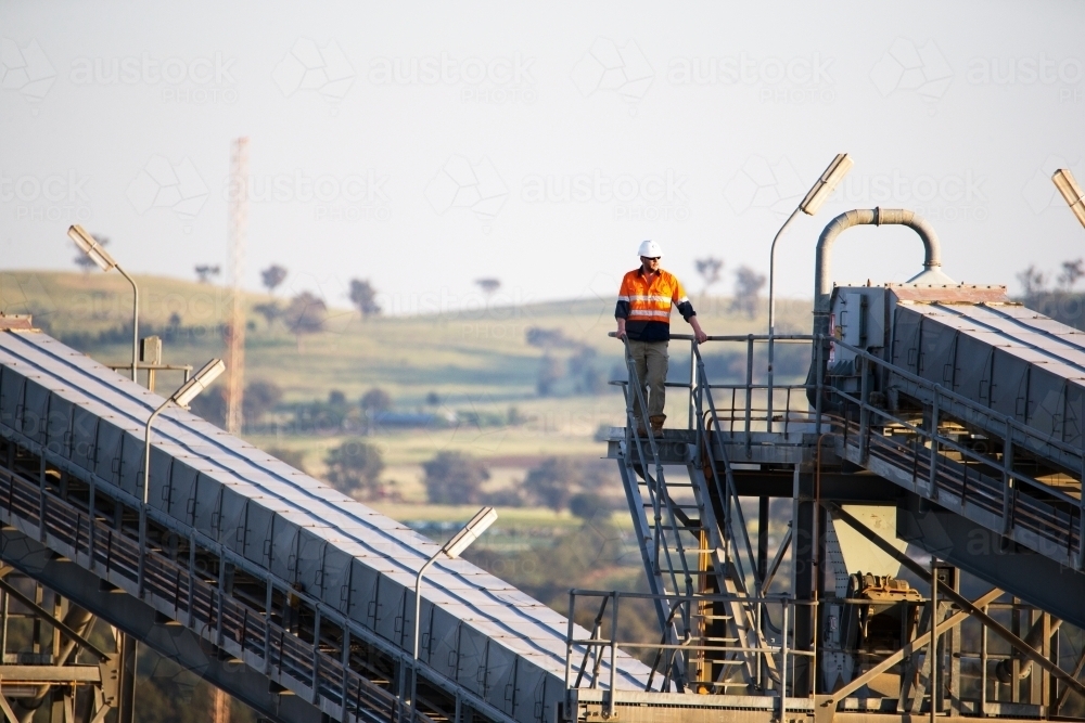 Worker wearing industrial safety vest with white helmet standing on a tall steel - Australian Stock Image