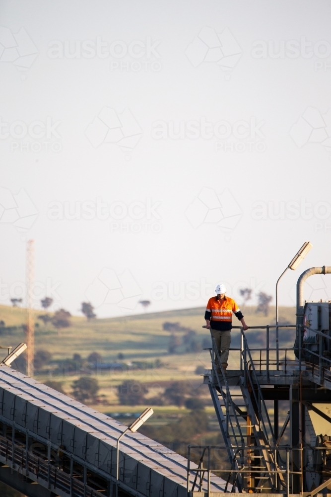 Worker wearing industrial safety vest with white helmet standing on a tall steel - Australian Stock Image