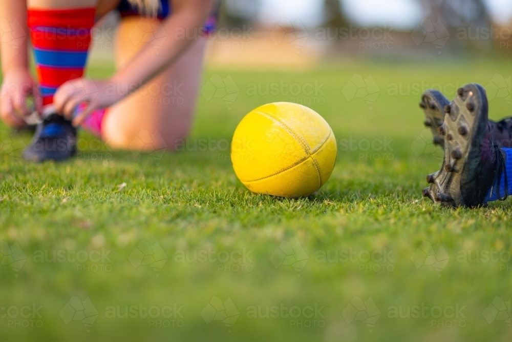 yellow afl football on green grass with detail of players boots - Australian Stock Image