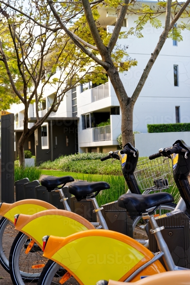 Yellow bikes for hire lined up on the side of the road at an inner-city street - Australian Stock Image
