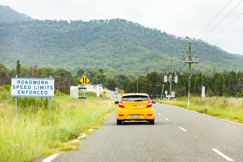 Yellow car driving down rural road on overcast day - Australian Stock Image