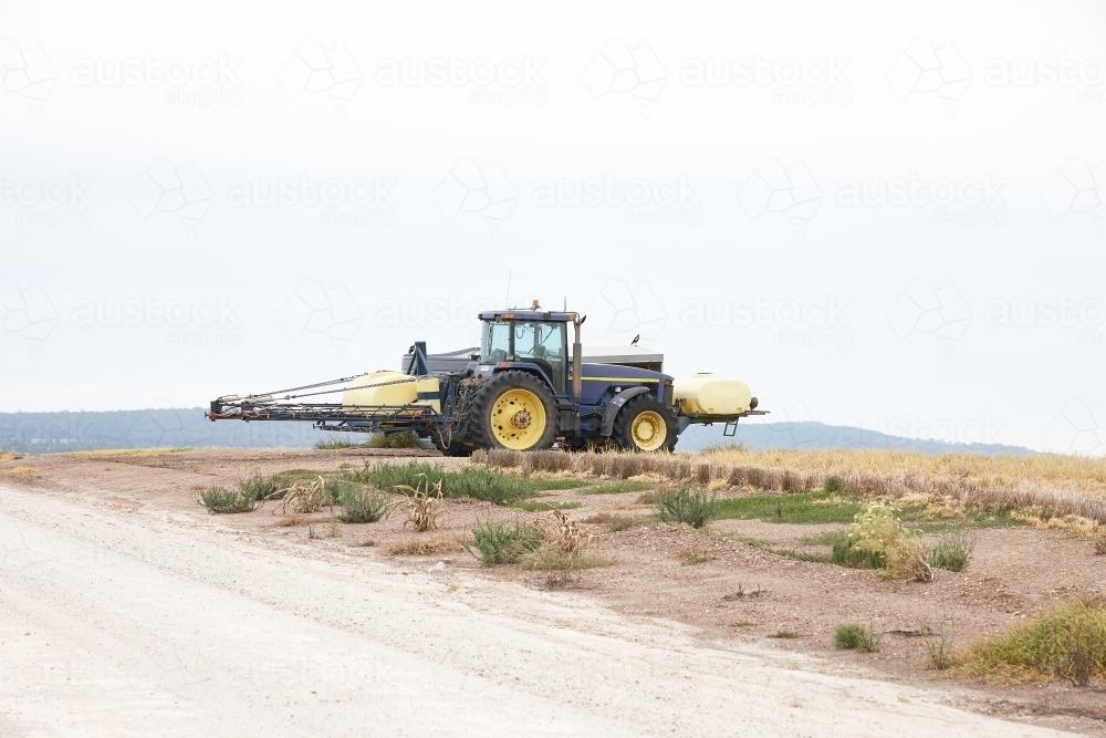 yellow tractor in an empty field and road - Australian Stock Image