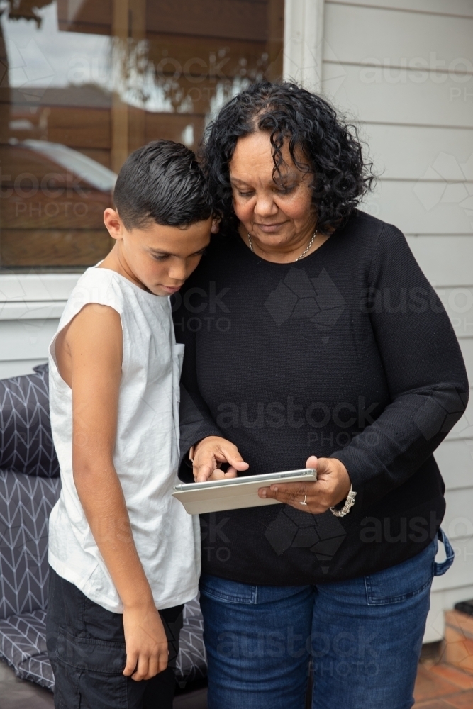 Young Aboriginal boy and Aboriginal woman looking at a device outside - Australian Stock Image