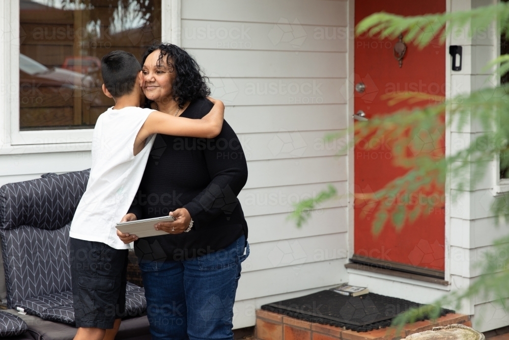 Young Aboriginal boy hugging Aboriginal woman on back porch - Australian Stock Image