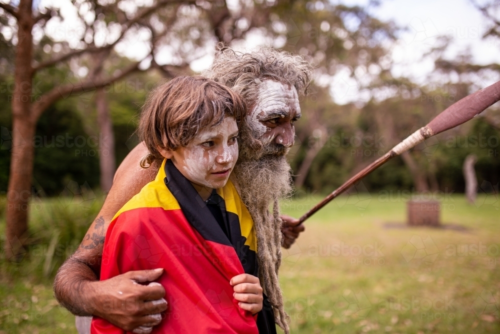 Young Aboriginal boy wearing the Aboriginal flag and being hugged by his father - Australian Stock Image