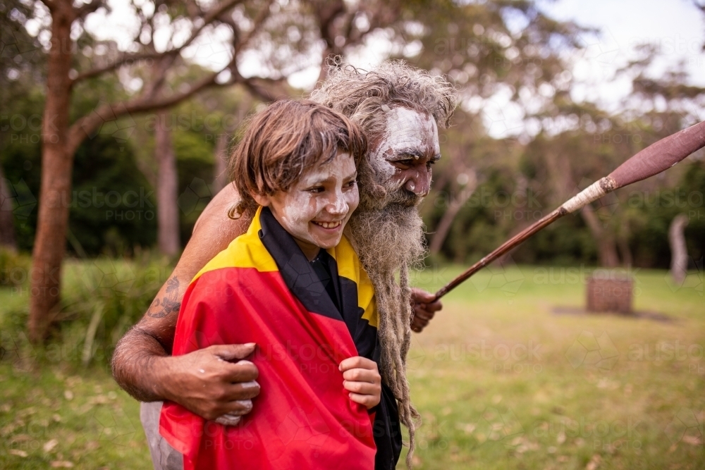 Young Aboriginal boy wearing the Aboriginal flag and being hugged by his father - Australian Stock Image