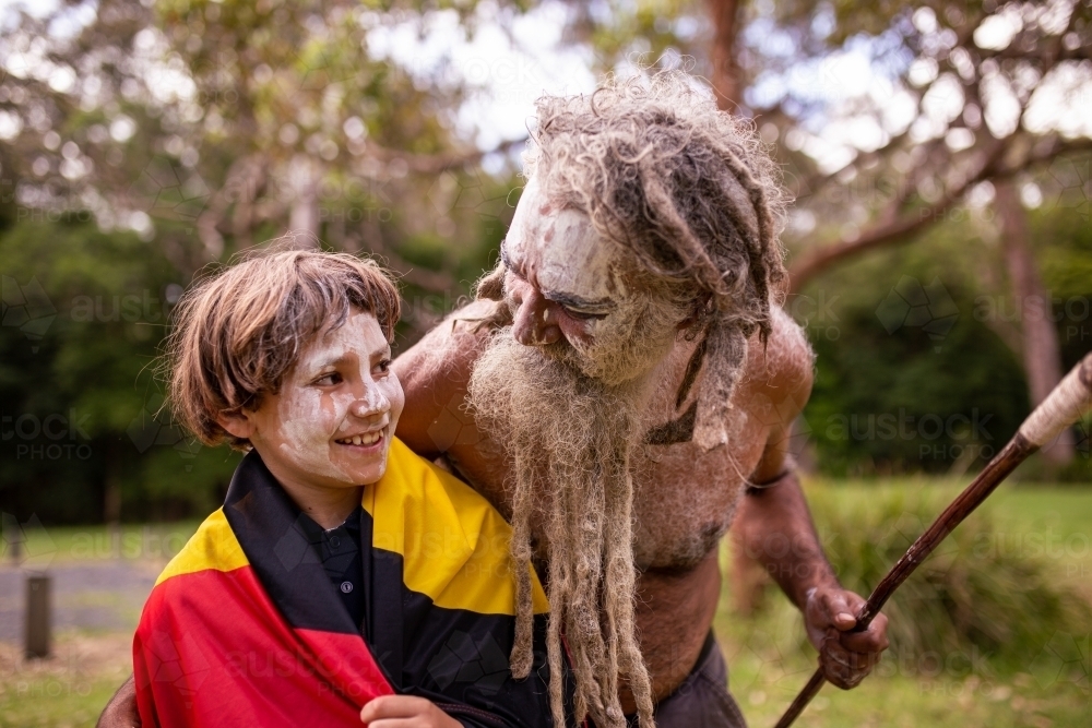 Young Aboriginal boy wearing the Aboriginal flag and being hugged. by his father - Australian Stock Image