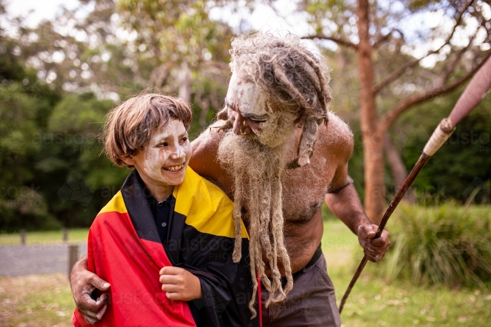 Young Aboriginal boy wearing the Aboriginal flag and being hugged by his father - Australian Stock Image