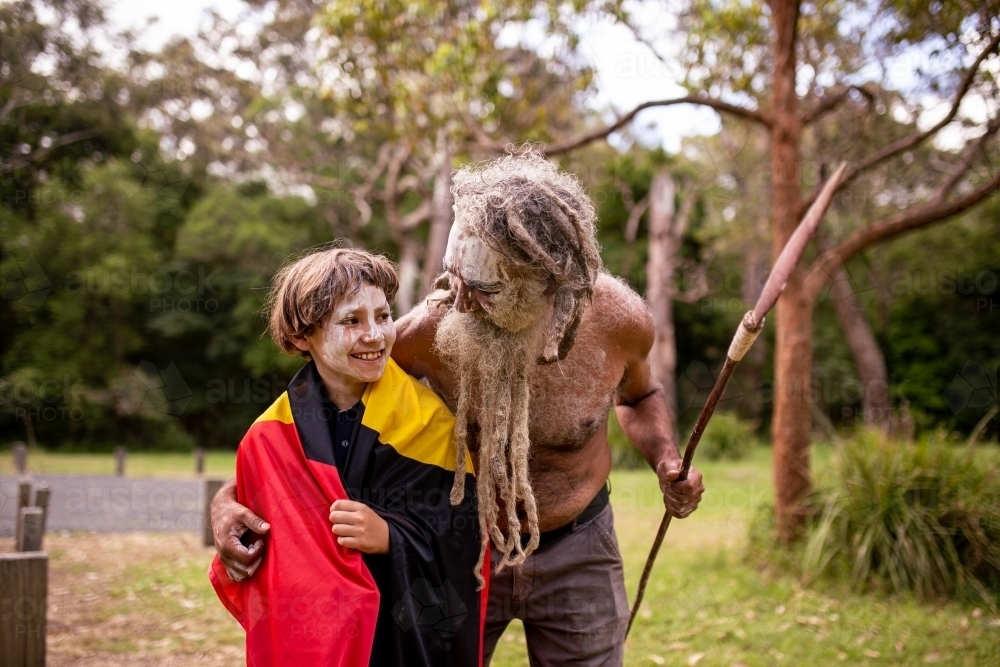 Young Aboriginal boy wearing the Aboriginal flag and being hugged by his father - Australian Stock Image