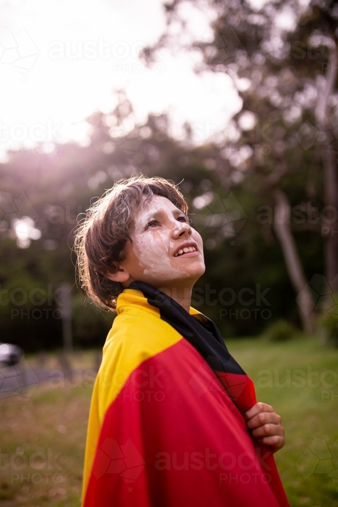 Young Aboriginal boy wearing the Aboriginal flag and smiling around his shoulders - Australian Stock Image