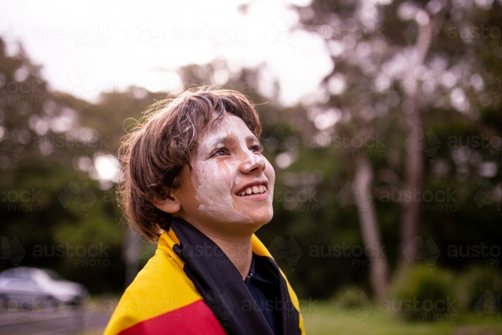 Young Aboriginal boy wearing the Aboriginal flag around his shoulders and smiling - Australian Stock Image