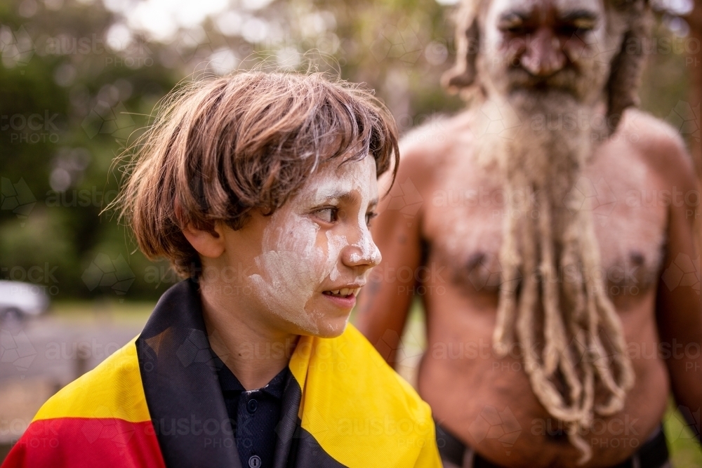 Young Aboriginal boy wearing the Aboriginal flag walking in front of his dad - Australian Stock Image