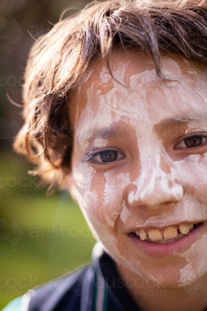 Young Aboriginal boy wearing white face paint smiling at the camera - Australian Stock Image